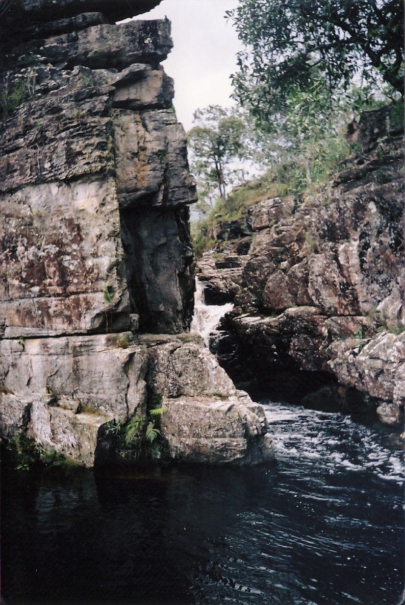a narrow gorge with a waterfall and a dark pool