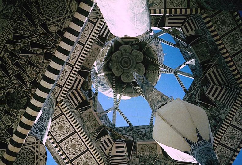 looking straight up inside a tower of black and white patterned panels to the blue sky