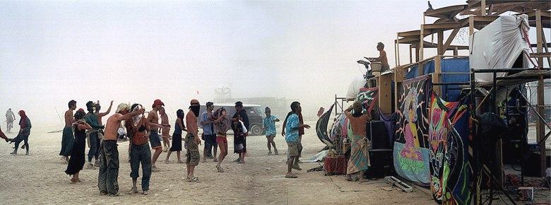 people dancing in the dust beside a scaffold hung with painted banners and speakers, a wide view in several frames