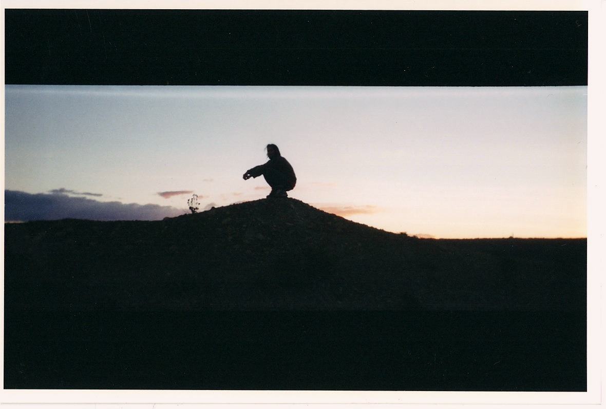 a silhouette crouching on a mound at dusk