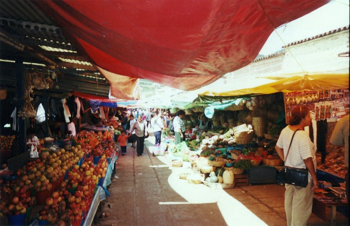 a market aisle under a red tarp, piles of oranges
