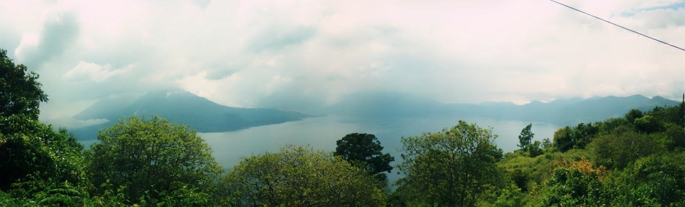 a volcano across a hazy blue lake from a green hillside