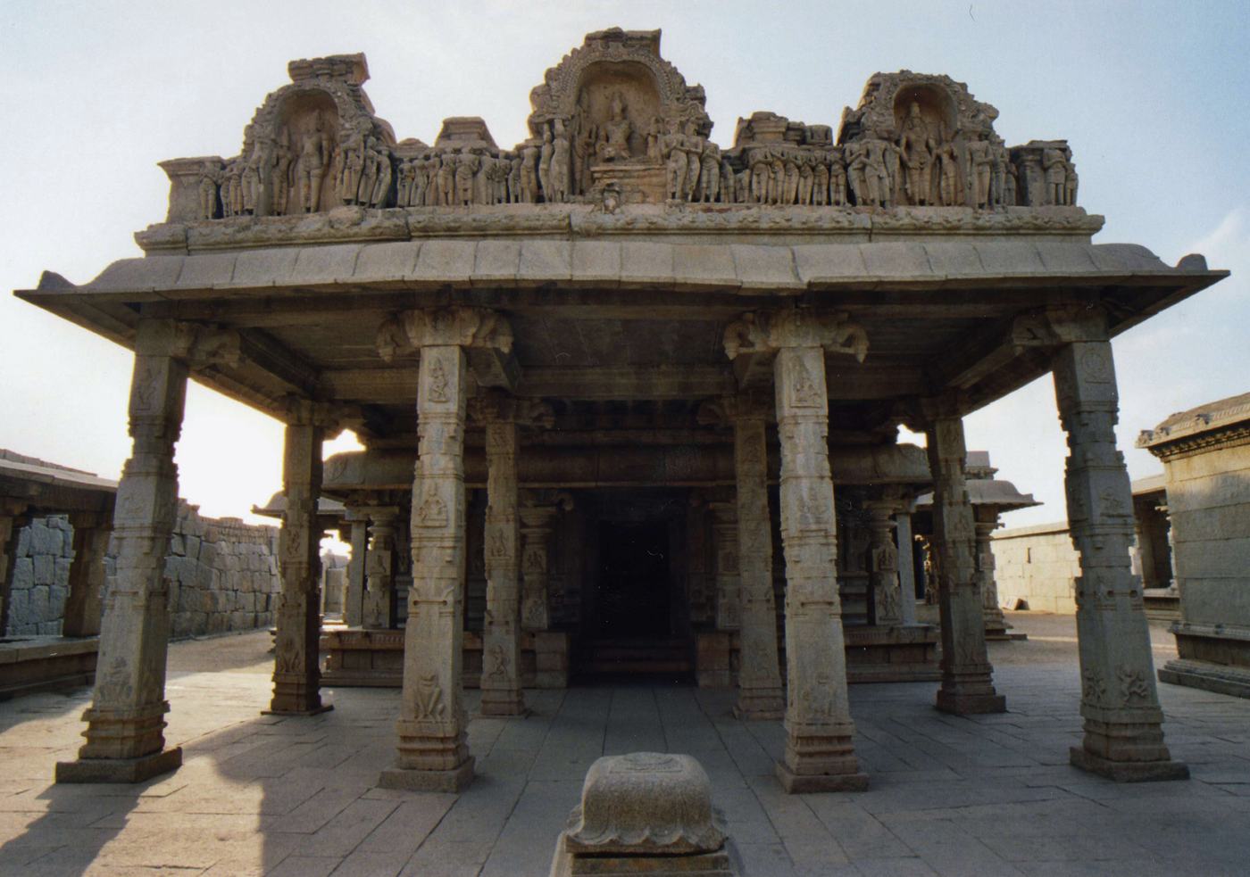 a stone pavilion on carved pillars, rows of carved figures along its roof, in a paved courtyard