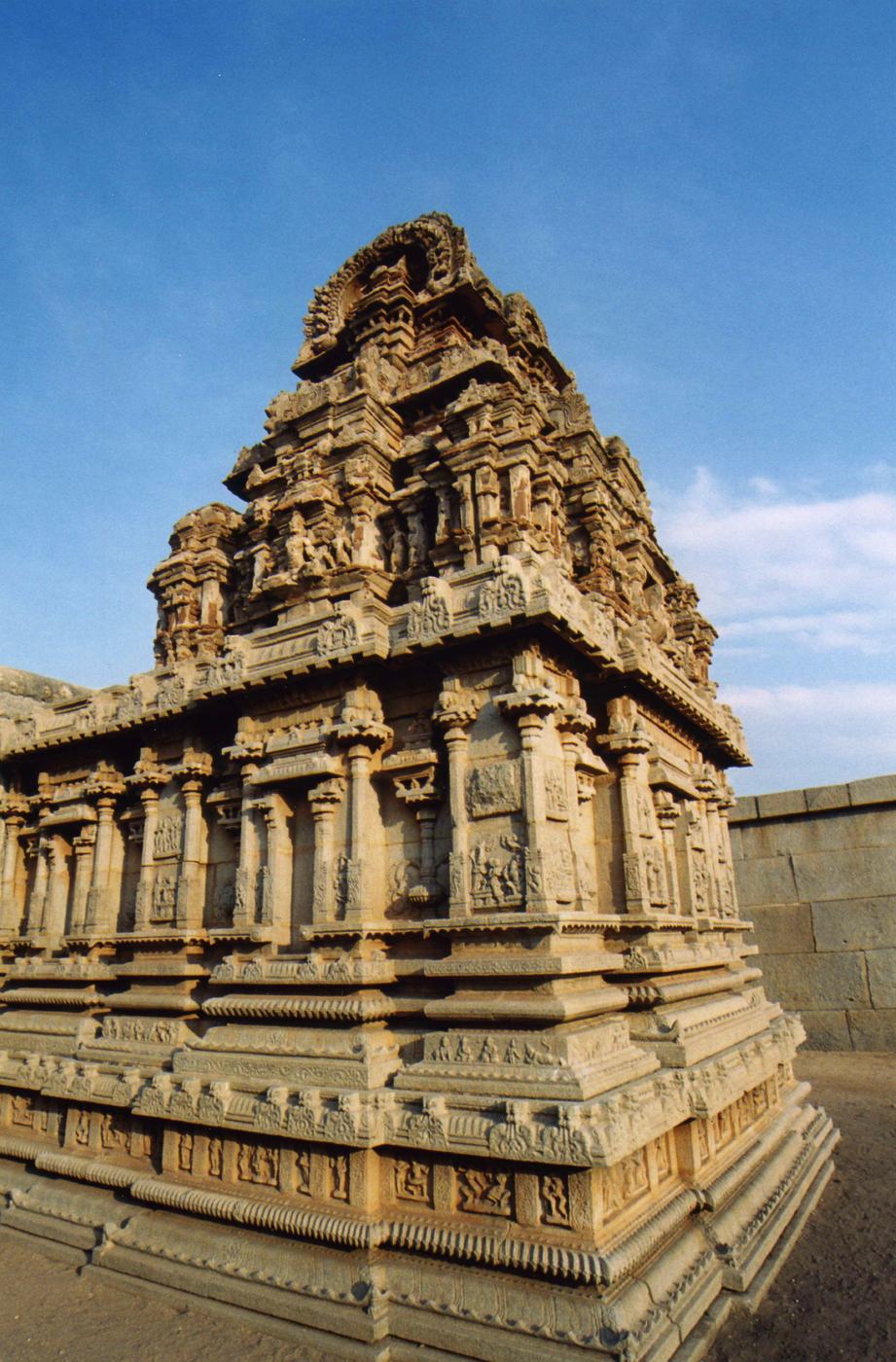 a temple tower covered in carved figures, seen from below against a blue sky