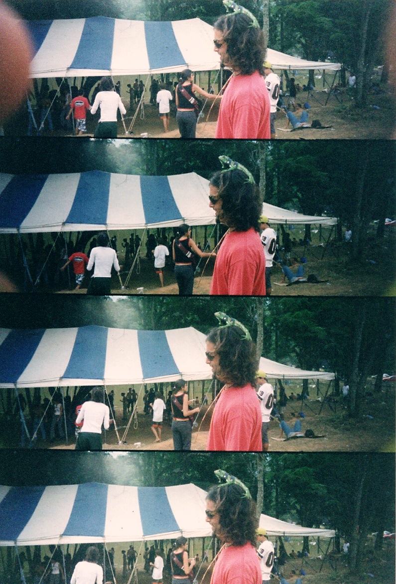 a man in red by a striped tent, a green lizard on his head