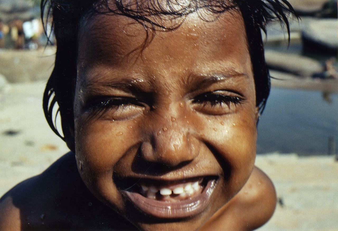 a wet child with a gap toothed grin, very close to the camera, water behind