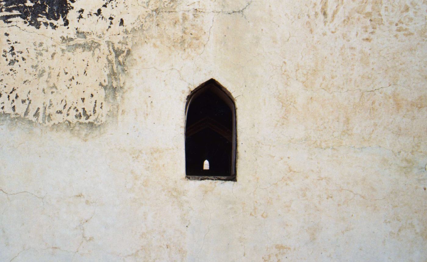 a small pointed window in a worn, peeling plaster wall