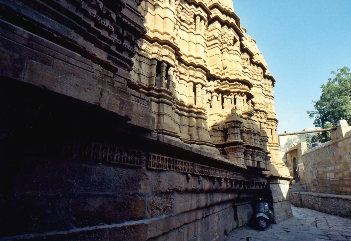 the carved sandstone wall and towers of a temple in a narrow lane, a scooter parked in its shadow