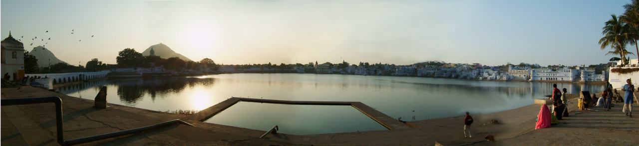 the lake at Pushkar under a low sun, white buildings along the far shore, people on the steps, a wide view in several frames