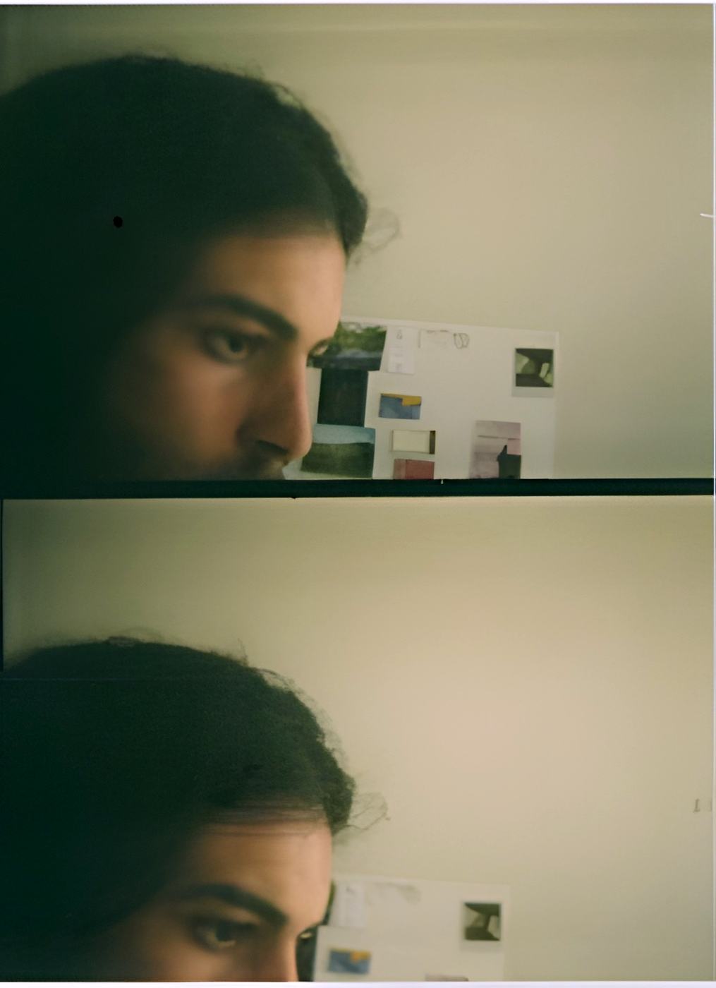a man in profile, pictures pinned to the wall behind him
