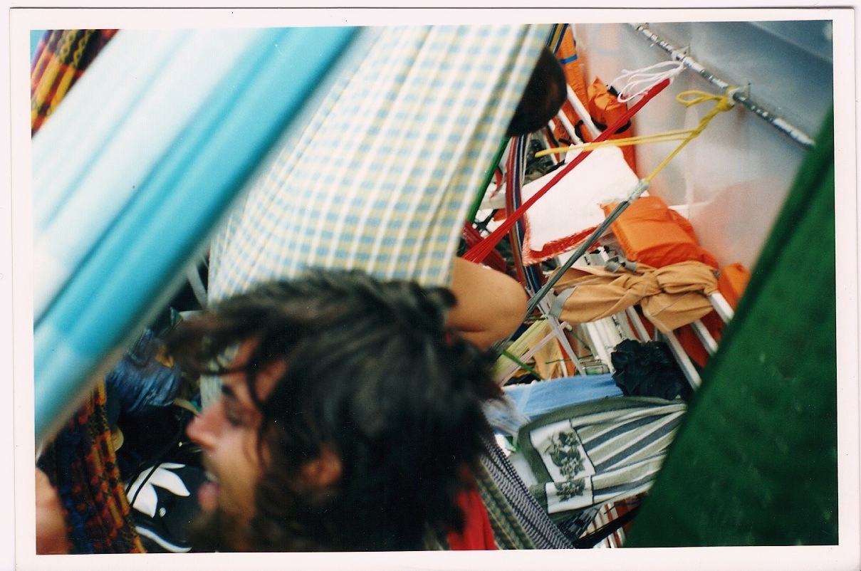 a bearded man laughing among hammocks, a checked one above him