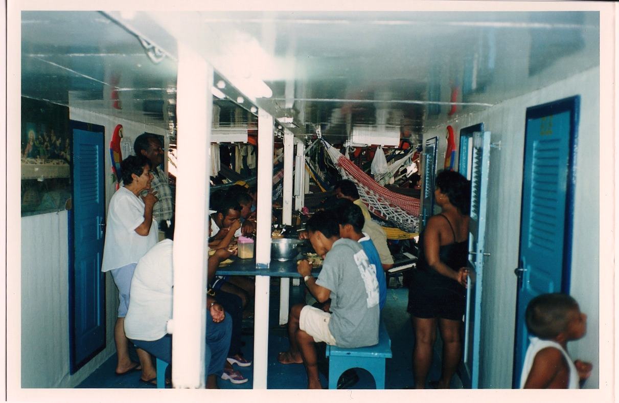 passengers eat at a table, hammocks hang behind