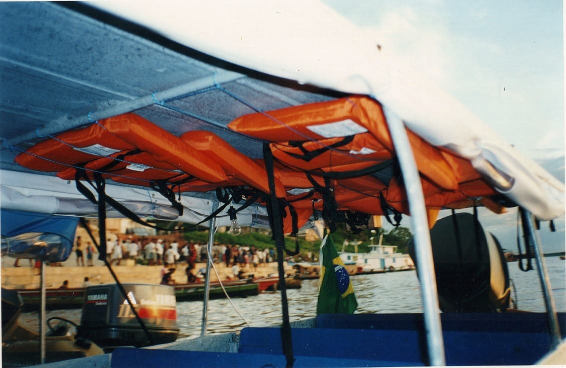 Orange life jackets hang under the canopy of a small boat, the crowded bank of an Amazon border town behind.