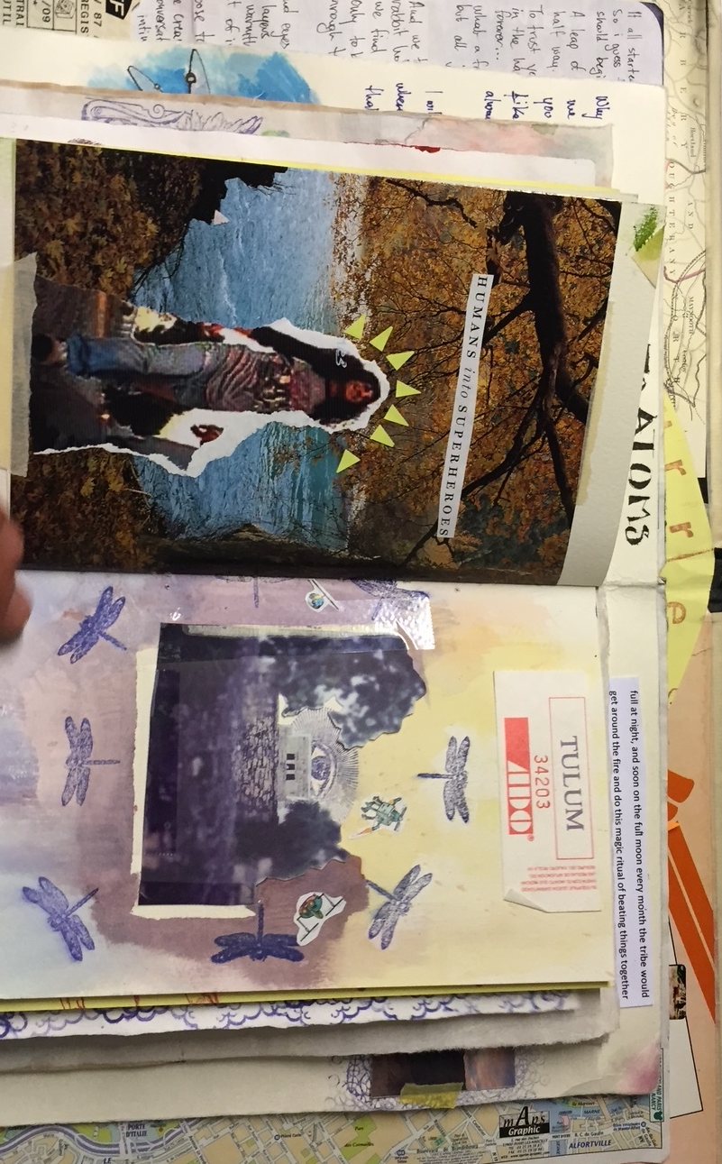 The open journal seen sideways: the Humans into superheroes collage above a page with a dark photograph, stamped blue dragonflies and a ticket marked Tulum.