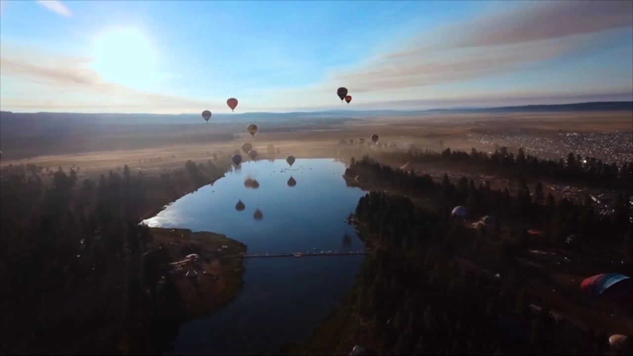 Hot air balloons drifting over a wide plain at dawn, a river winding below, the sun rising.