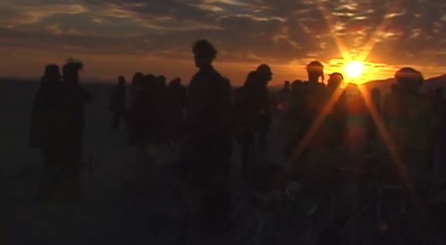 Dark figures against a desert sunset, the sun a white flare on the horizon.