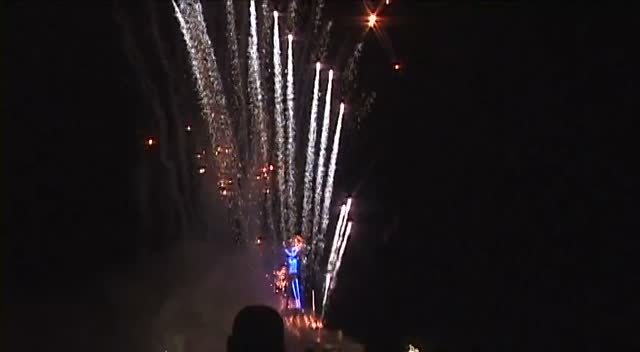 Fireworks streaming down through black night above a small lit figure.