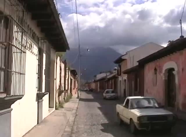 A narrow street of painted colonial houses under a storm sky, a car parked at the kerb.