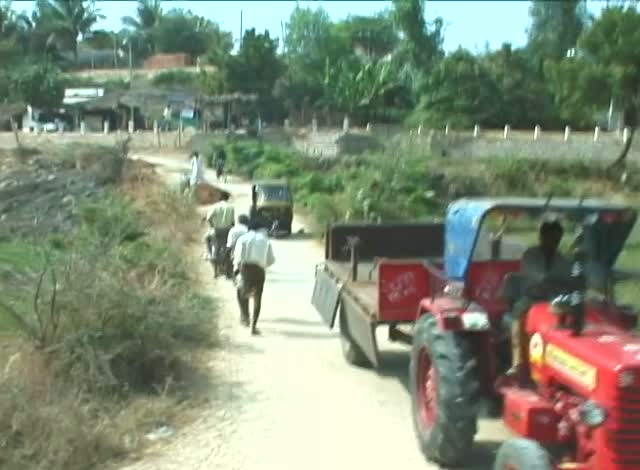 A red tractor on a dirt road between green hills, a man walking beside it.