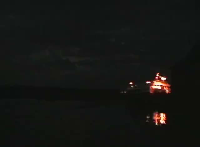 A boat lit up at night on a dark river, its lights doubled in the water, a frame from the tape.