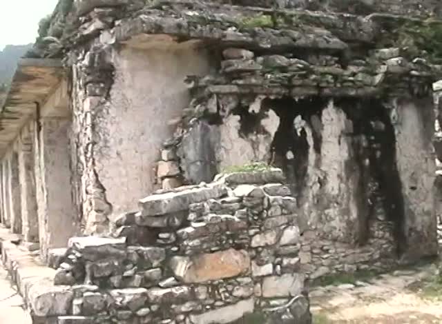 A stone corridor of Maya ruins, thick walls and lintels under trees.