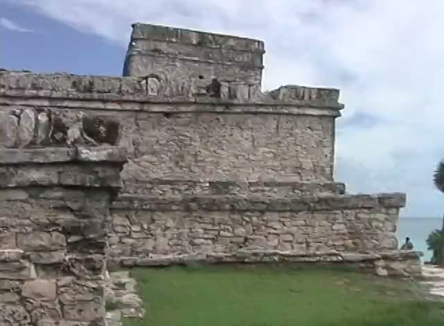 The stone temple at Tulum under a cloudy sky, grass at its foot and the sea beyond, a frame from the tape.