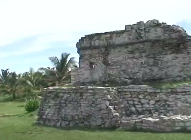 The Castle at Tulum, a grey stone temple on its mound against a blue sky, a palm beside it.